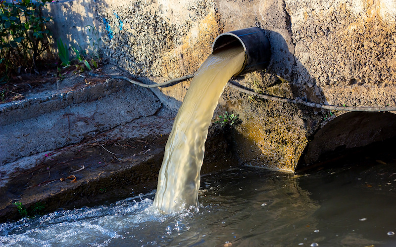 Wastewater sewage pipe dumps the dirty contaminated water into the river. Water pollution, environment contamination concept.