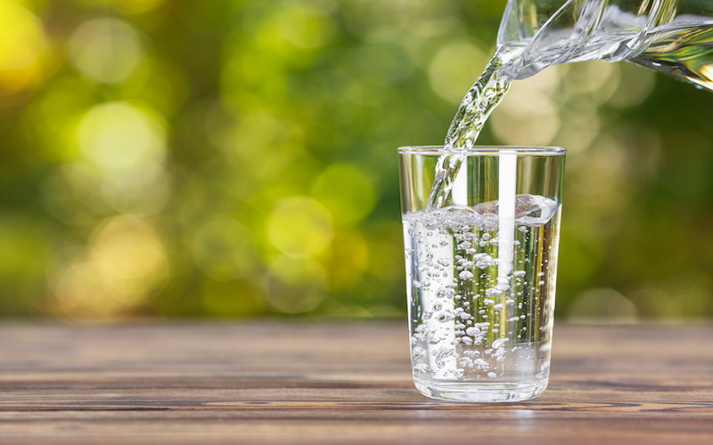 water from jug pouring into glass on wooden table outdoors